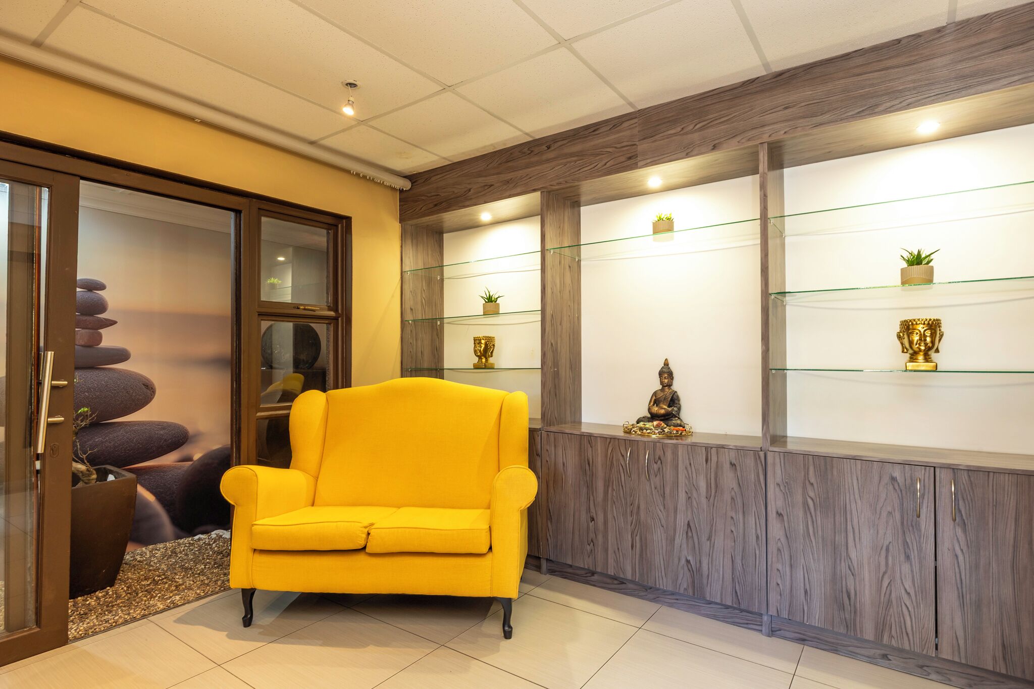 A modern interior with a yellow armchair, glass shelves with decorative items, and a stone arrangement.