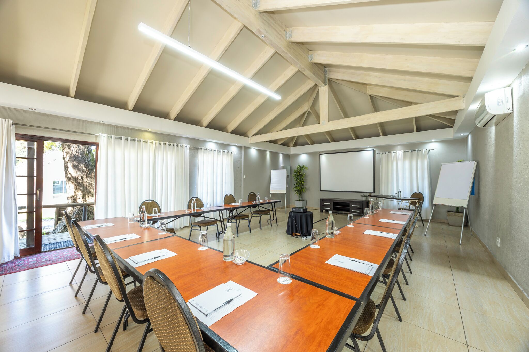 A conference room with a long wooden table, chairs, a projector screen, and a whiteboard.