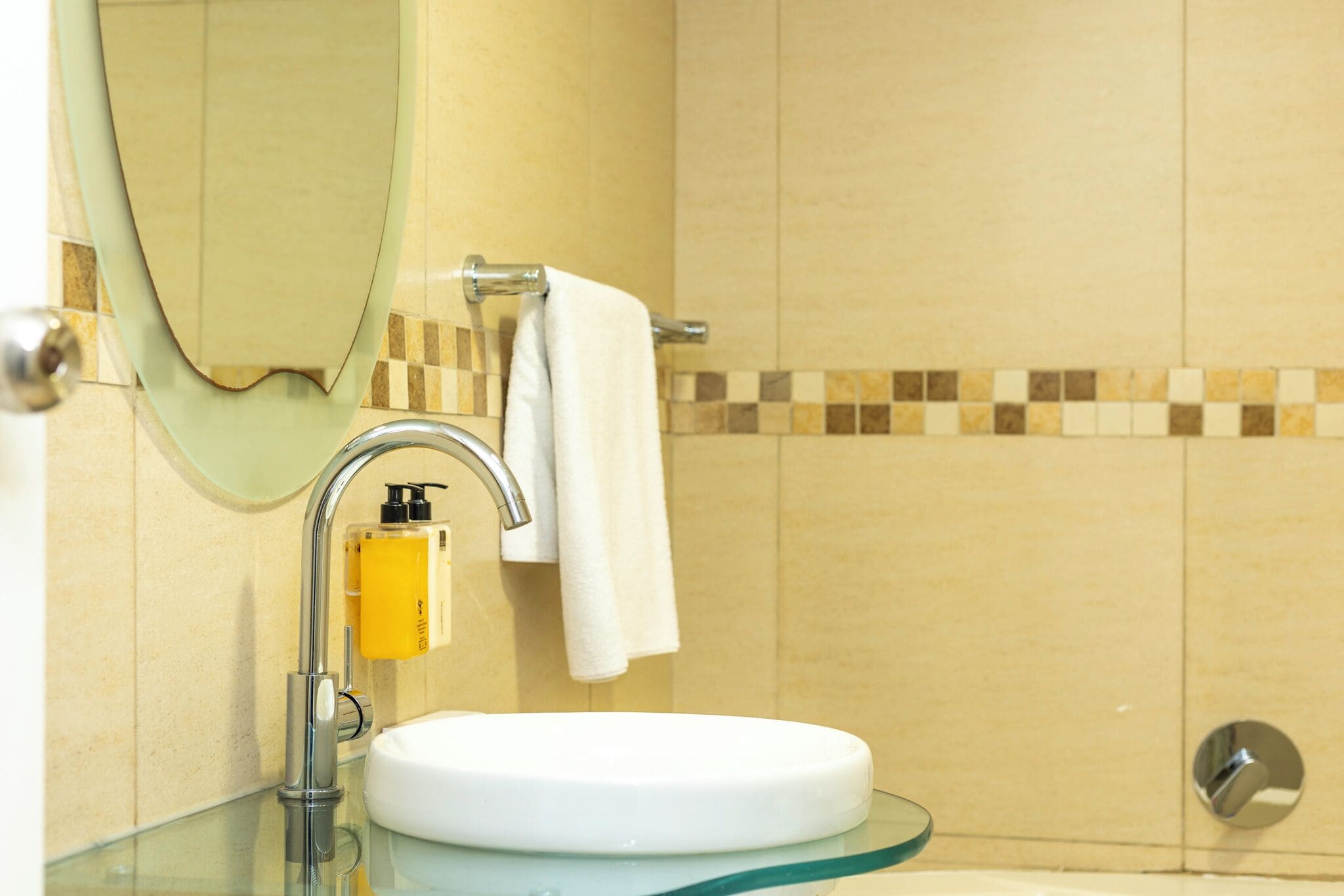 A bathroom with a glass sink, a mirror, a towel rack, and a shower area.