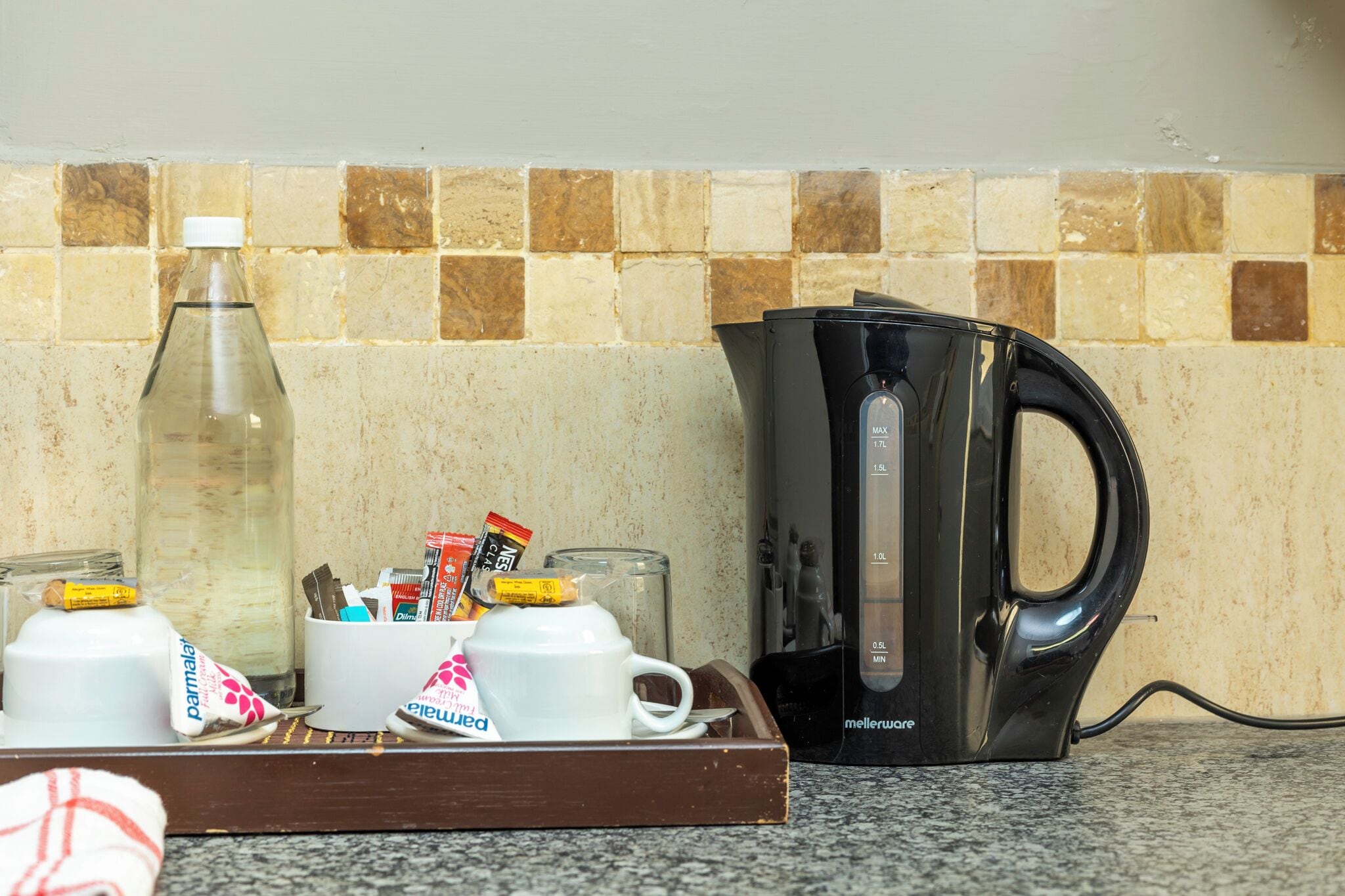 A kitchen counter with a coffee maker, a glass of water, and a tray with cups and condiments.