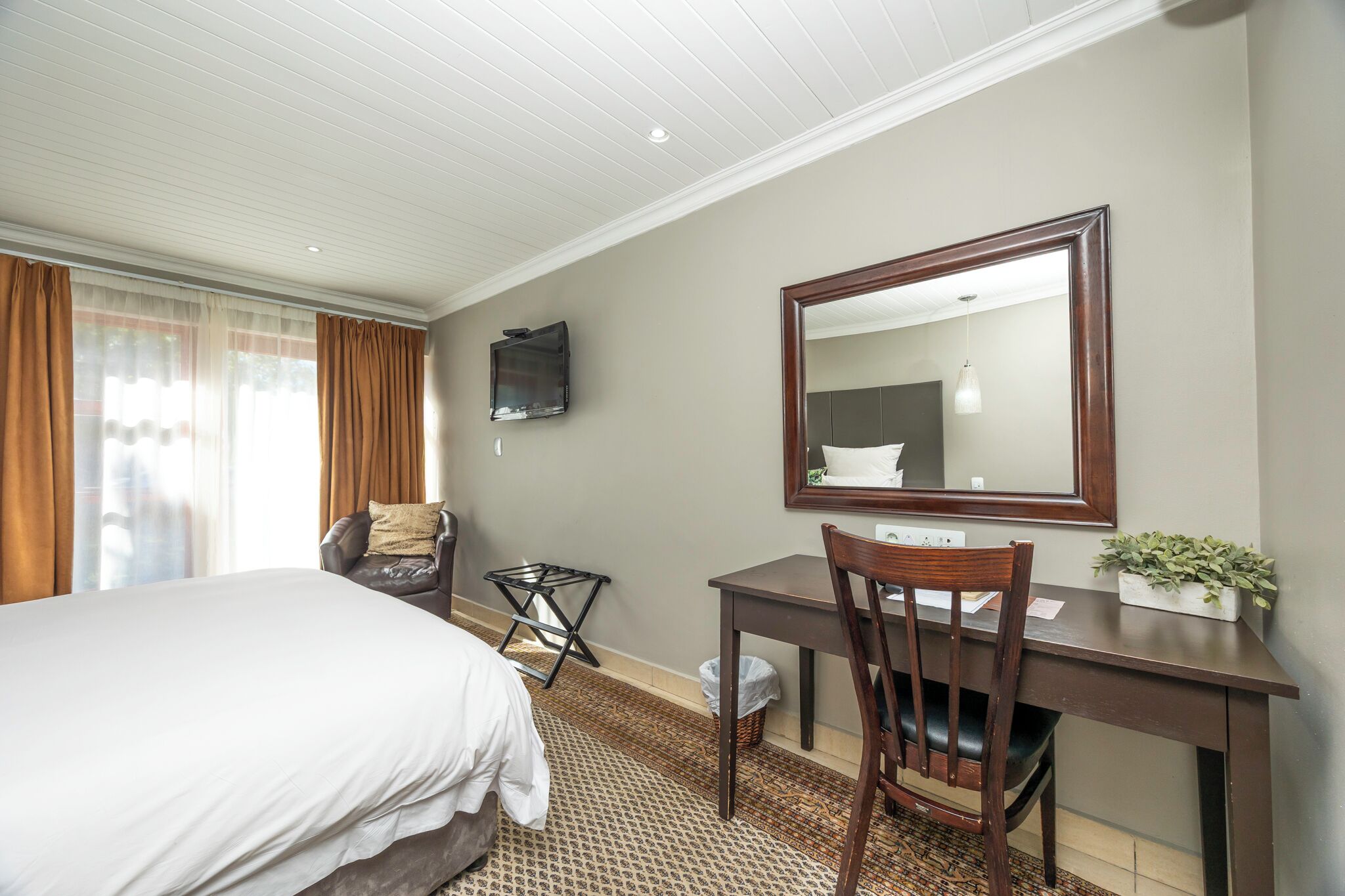 A hotel room with a bed, a desk, a chair, a television, and a mirror.