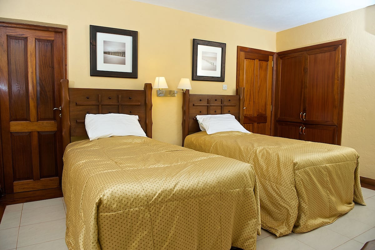 A hotel room with two beds, wooden wardrobes, and framed pictures on the wall.
