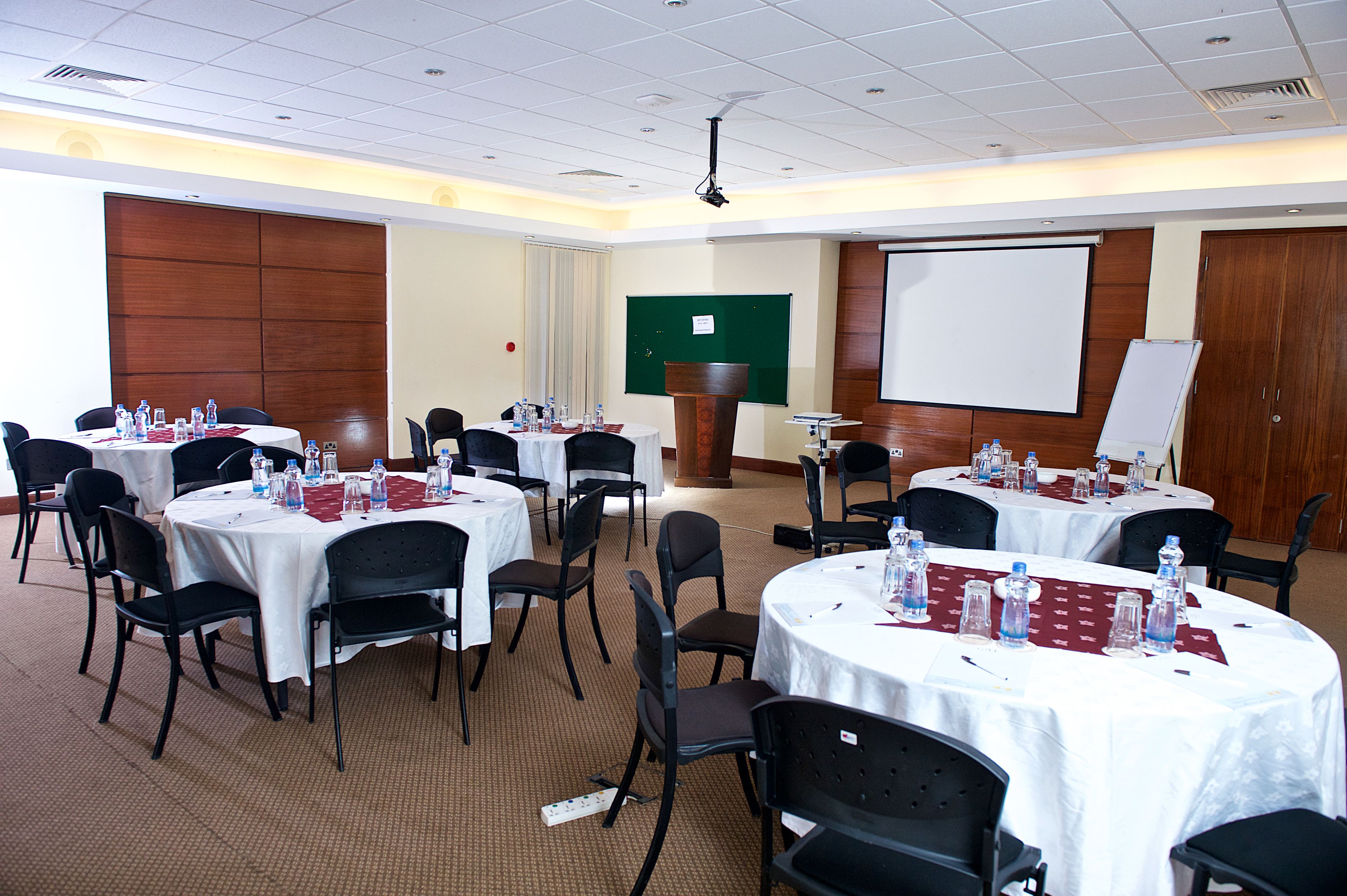 A conference room with multiple tables, chairs, and a projector screen.