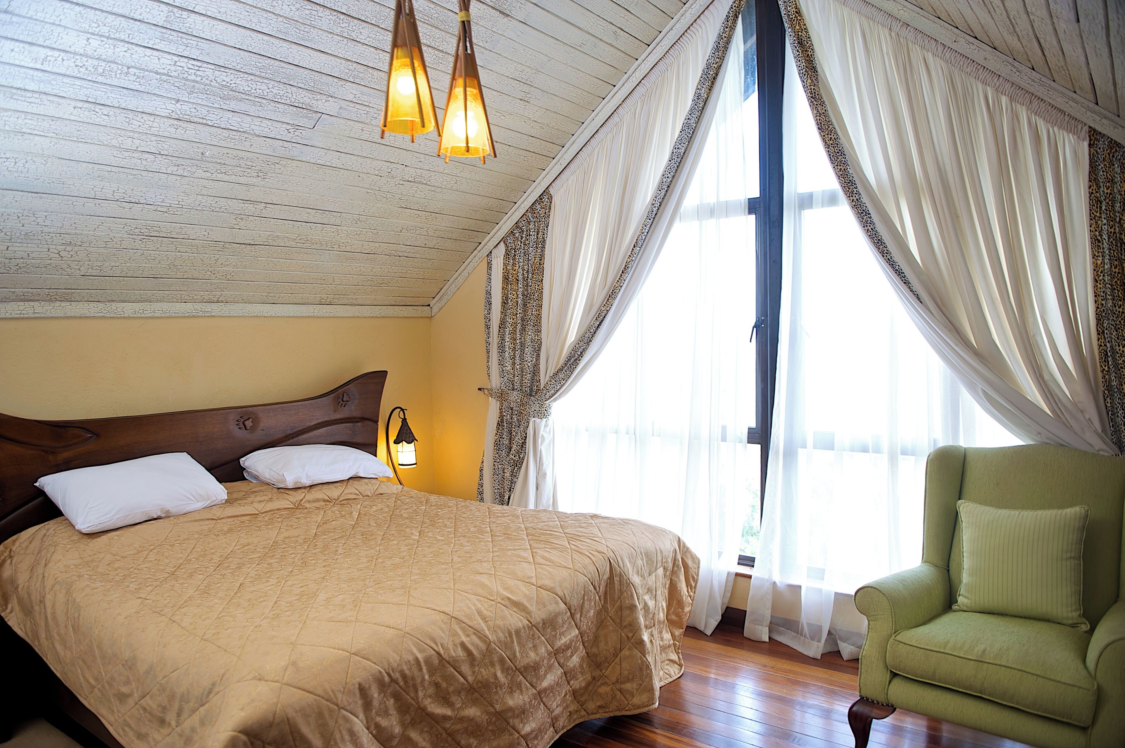 A bedroom with a large bed, a green armchair, and a window with curtains.