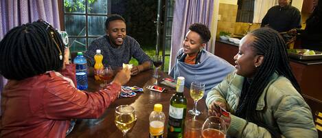Un grupo de personas sentadas alrededor de una mesa, con bebidas y cartas, en una habitación con ventana y cortinas.