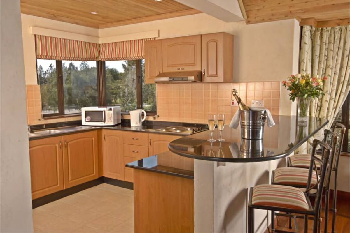A kitchen with wooden cabinets, a microwave, a coffee maker, a glass of champagne, and a dining area with striped chairs.