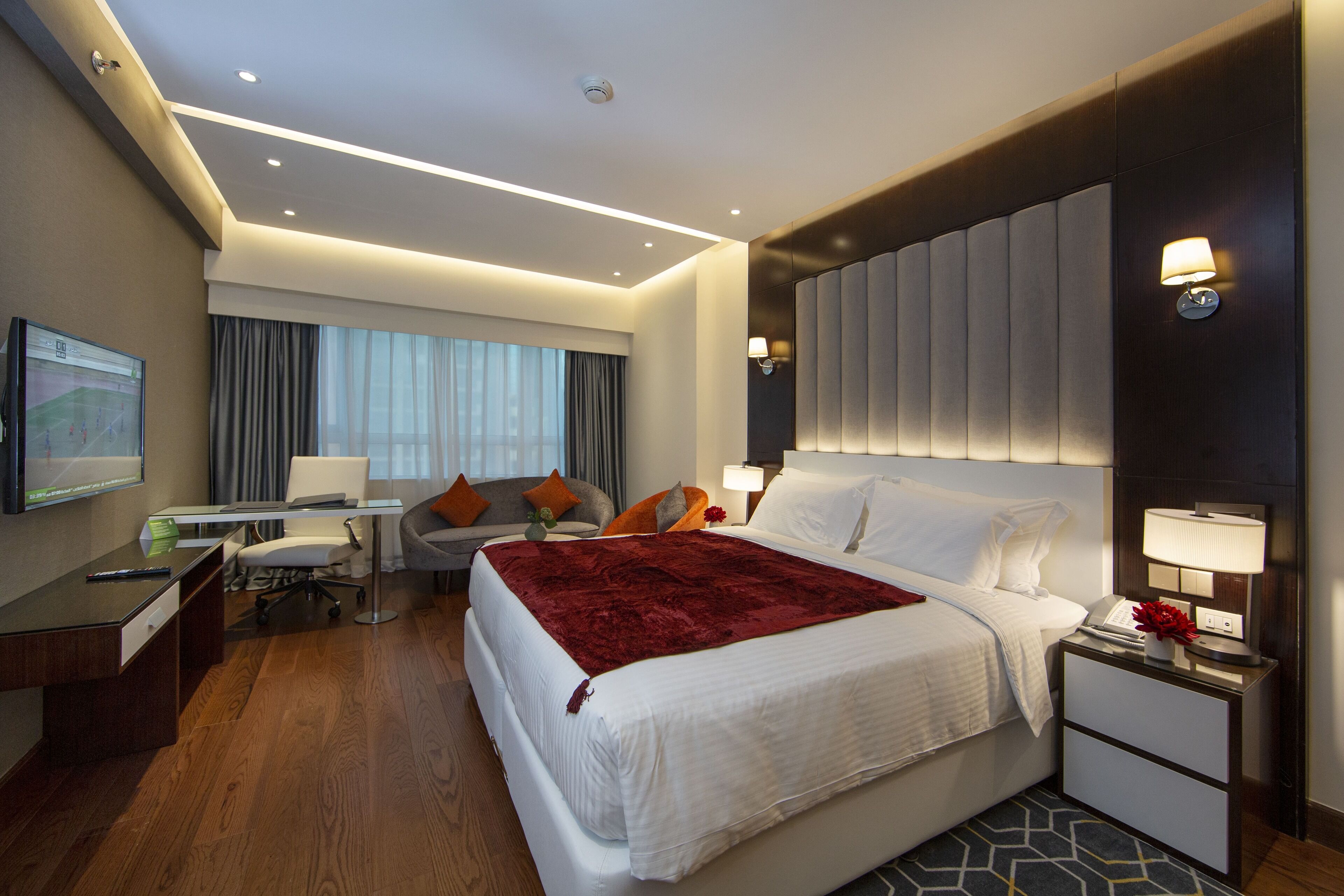 A hotel room with a large bed, a desk, a chair, a TV, and a window with curtains.