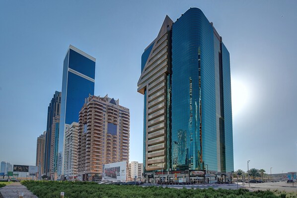 A cityscape with modern high-rise buildings, including a prominent blue glass skyscraper and a beige building with a unique design. - Number One Tower Suites (Dubai)