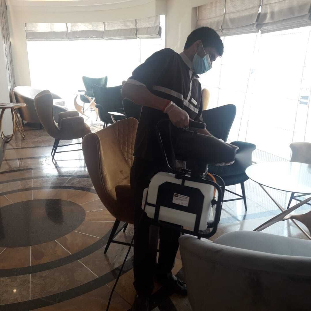 A person adjusting a suitcase in a room with a tiled floor, several chairs, and a large window.