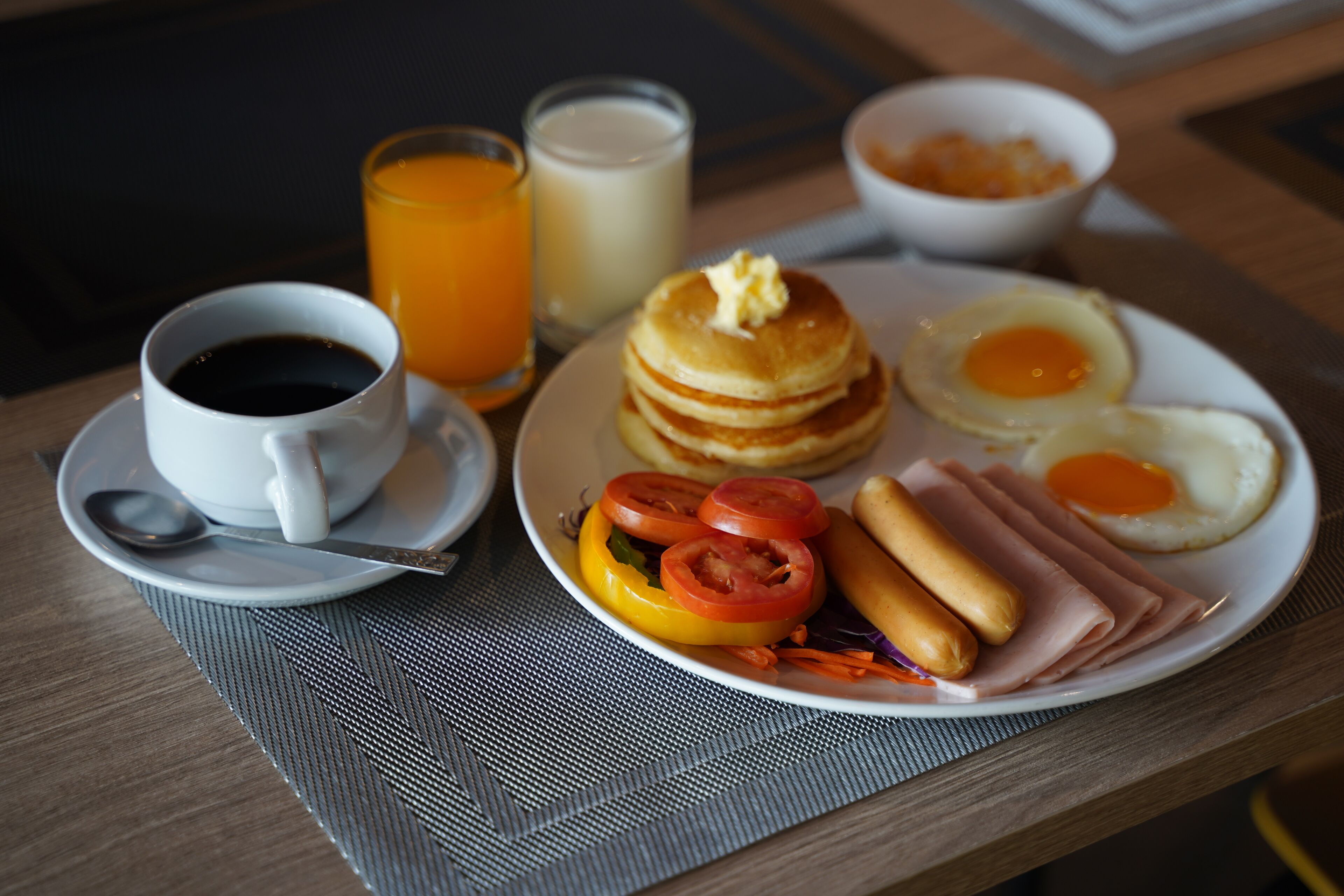 Une assiette de petit-déjeuner avec des crêpes, des œufs, du jambon et des tomates.