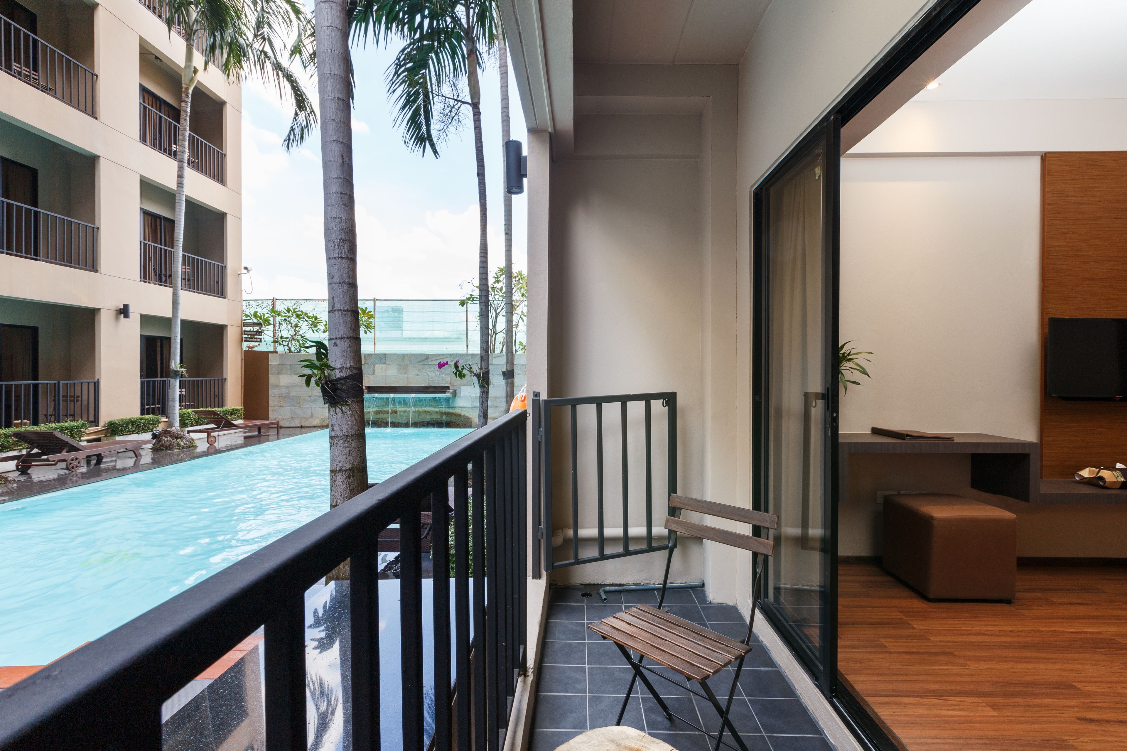 Uma varanda com vista para uma piscina, um banco de madeira e uma porta de vidro que dá para um quarto com uma TV e uma pequena mesa.