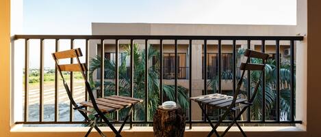A balcony with two wooden chairs and a small table, a tree stump, and a view of palm trees and buildings.