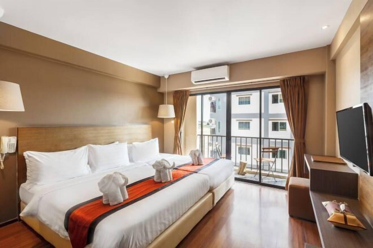 Ein Hotelzimmer mit Bett, Fernseher, Balkon und Blick auf Gebäude, sowie einer Klimaanlage.