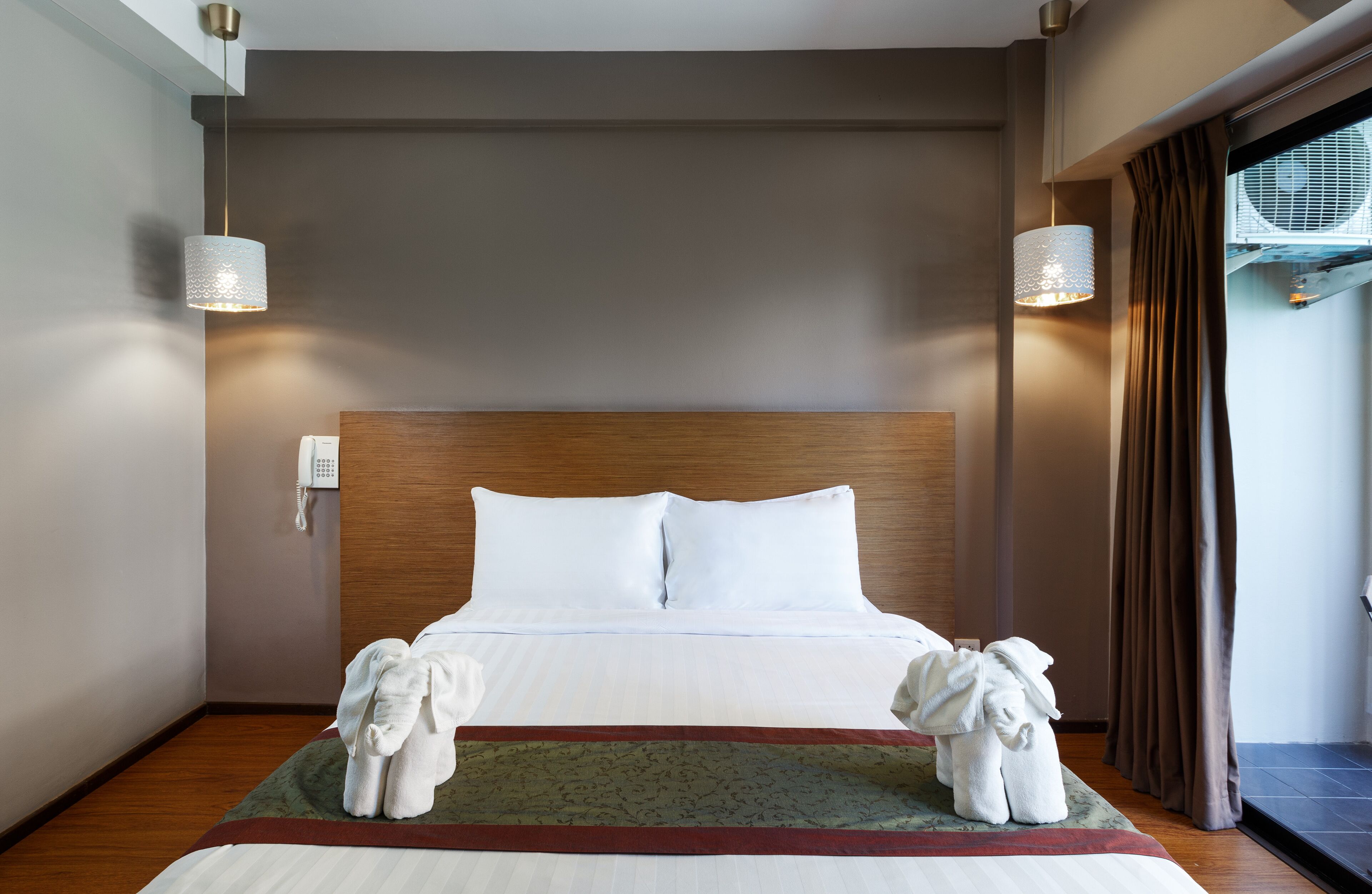 Habitación de hotel con una cama grande, dos lámparas de noche, un teléfono y una ventana con cortinas.