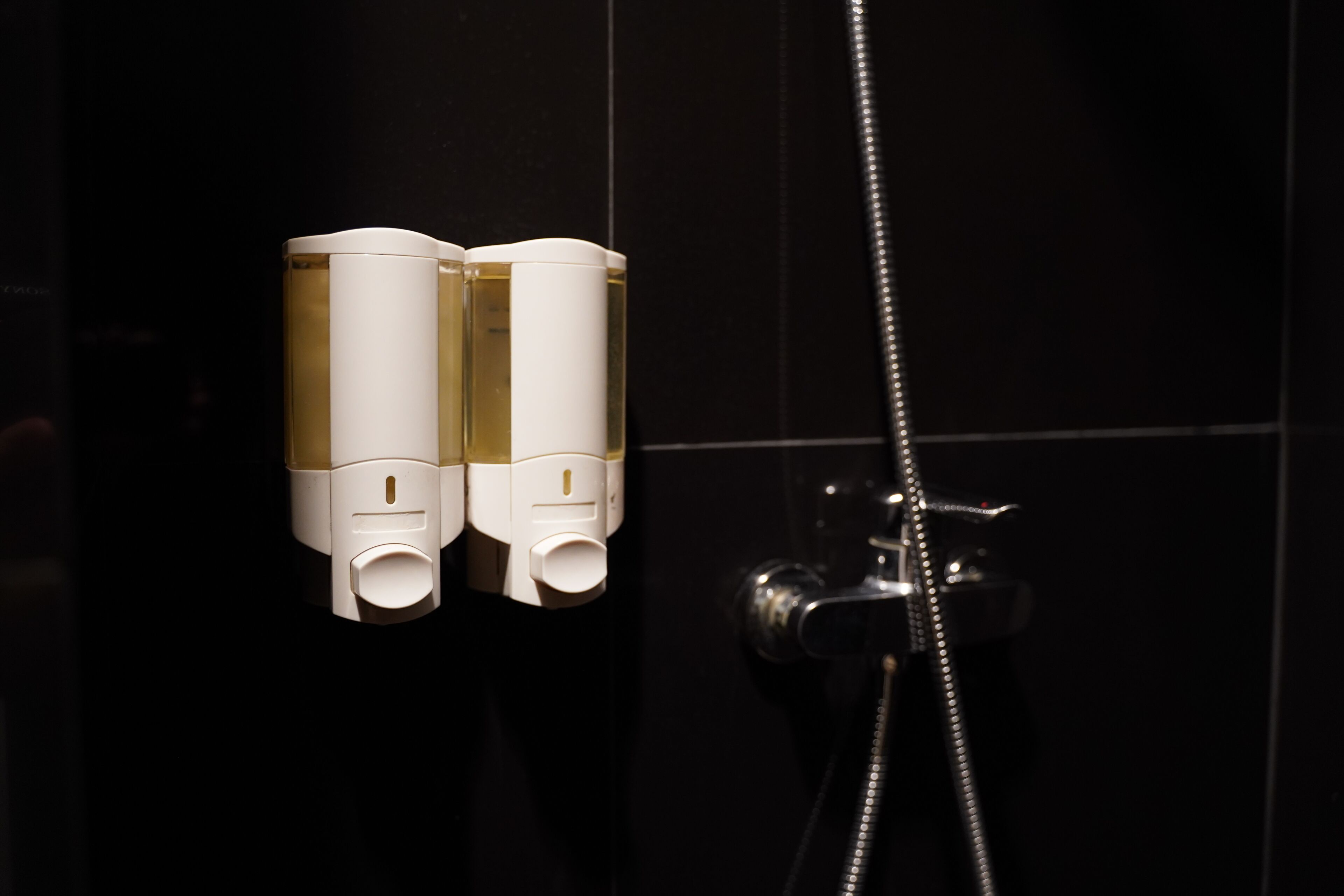 A bathroom with a black tiled wall and a shower with a silver hose.