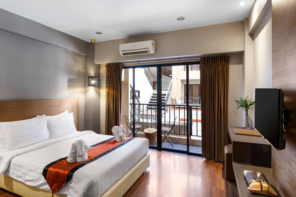 Ein Hotelzimmer mit einem großen Bett, einem Flachbildfernseher, einem kleinen Tisch mit einer Pflanze und einem Balkon mit Blick ins Freie.