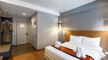 A hotel room with a bed, a bedside table, a hanging coat rack, and a wall-mounted telephone.