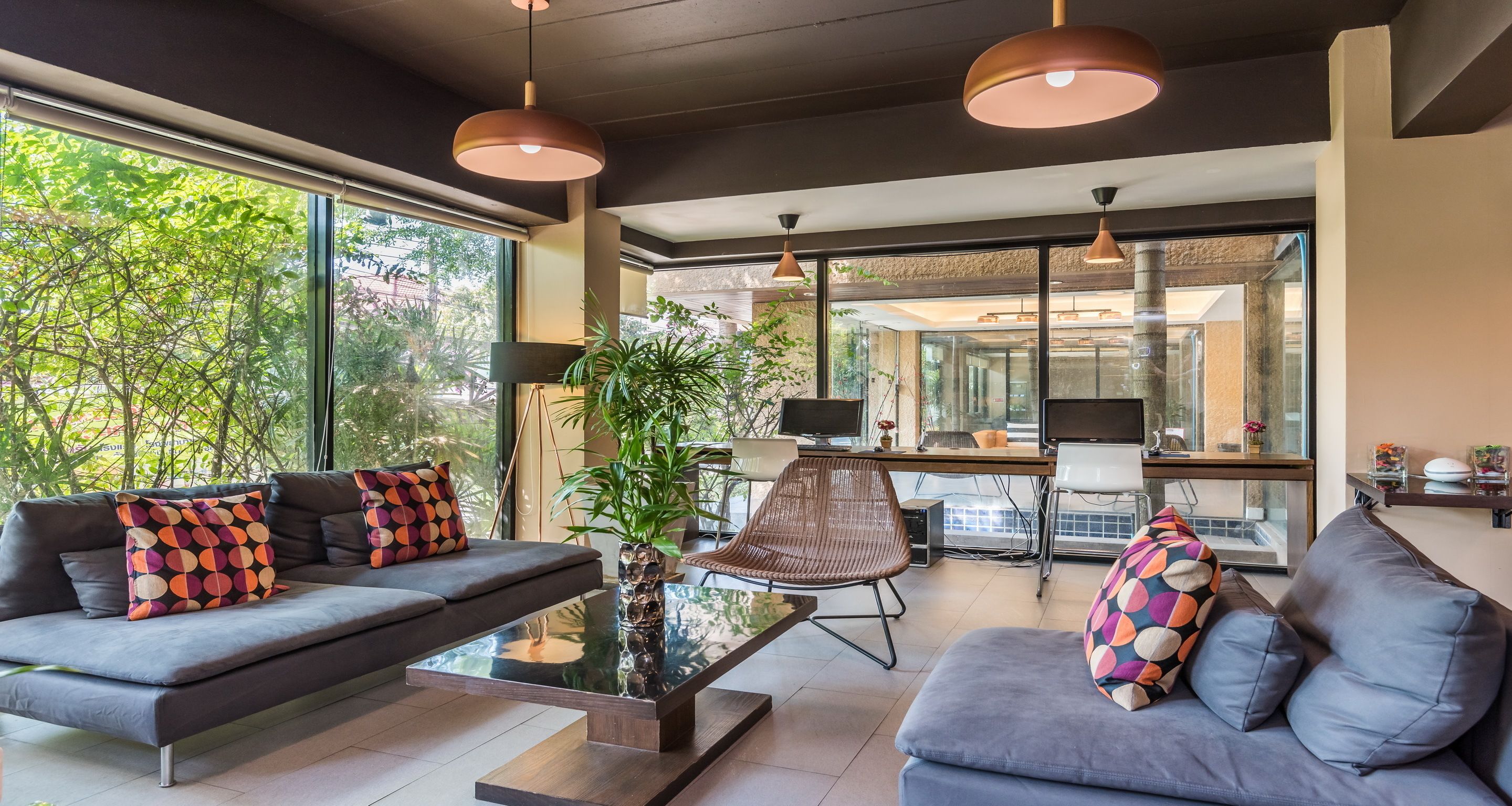 Een moderne woonkamer met een bank, salontafel en stoelen. Een groot raam met uitzicht op bomen.