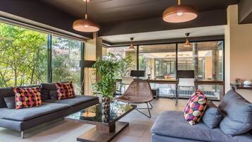 Een moderne woonkamer met een bank, salontafel en stoelen. Een groot raam met uitzicht op bomen.