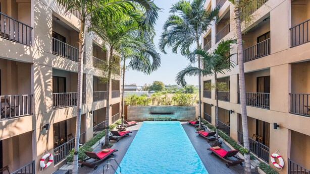 Un hotel de varios pisos con piscina central, balcones y palmeras.