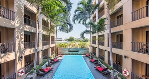 A multi-story hotel with a central swimming pool, balconies, and palm trees. - The Cottage Suvarnabhumi (Bangkok)