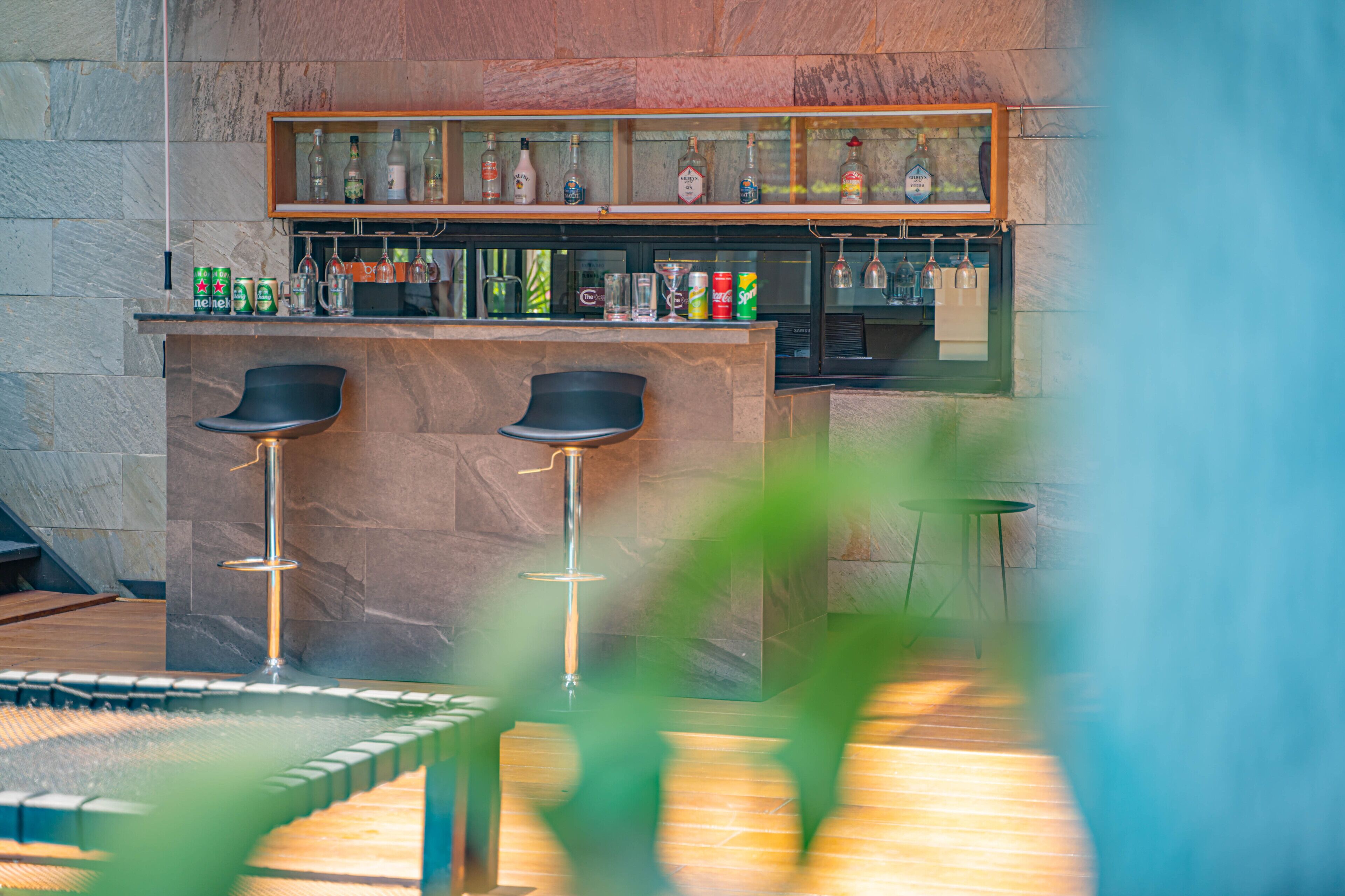 Zona de bar con pared de mármol, estanterías con botellas y dos taburetes negros.
