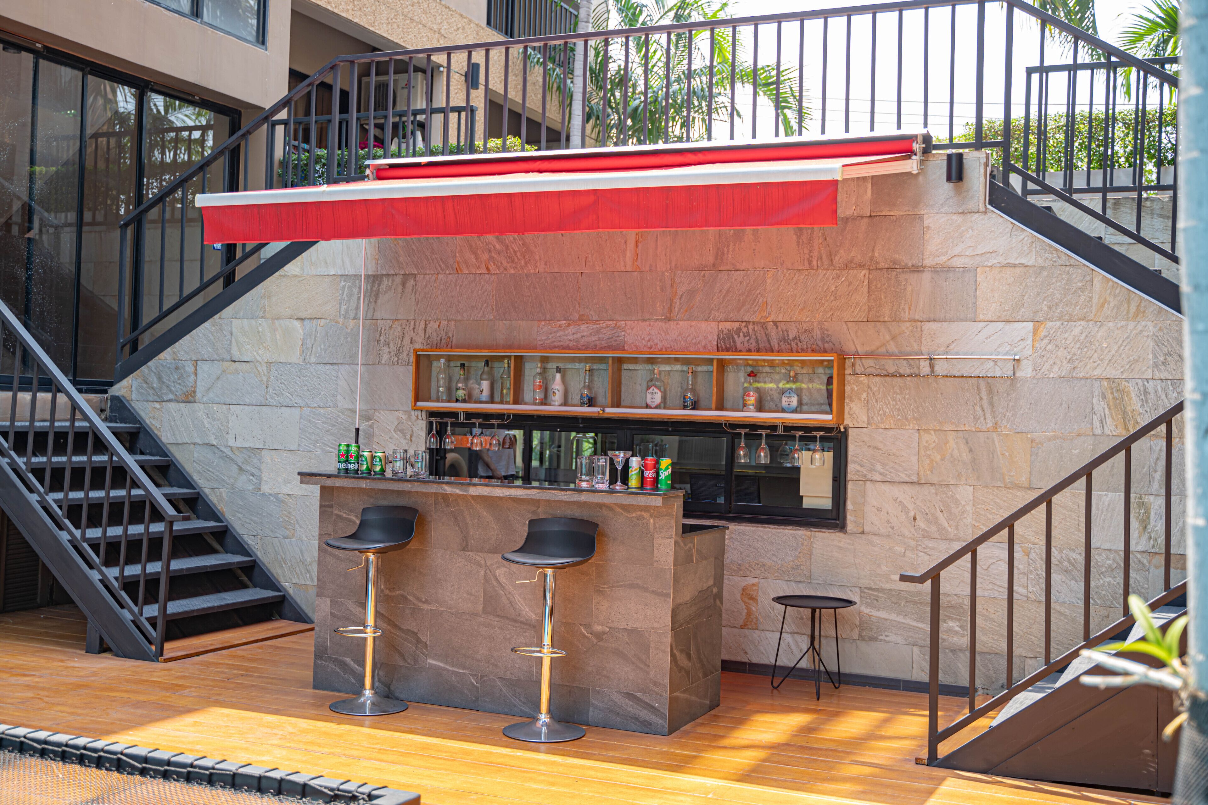 Zona de bar con pared de piedra, dos taburetes y una barra con botellas, además de una escalera.