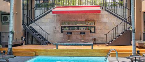 Un área de piscina con un bar, dos sillas y una escalera que lleva a un nivel superior.