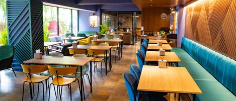 A modern restaurant with wooden tables and blue booths, featuring a geometric wall design and large windows.
