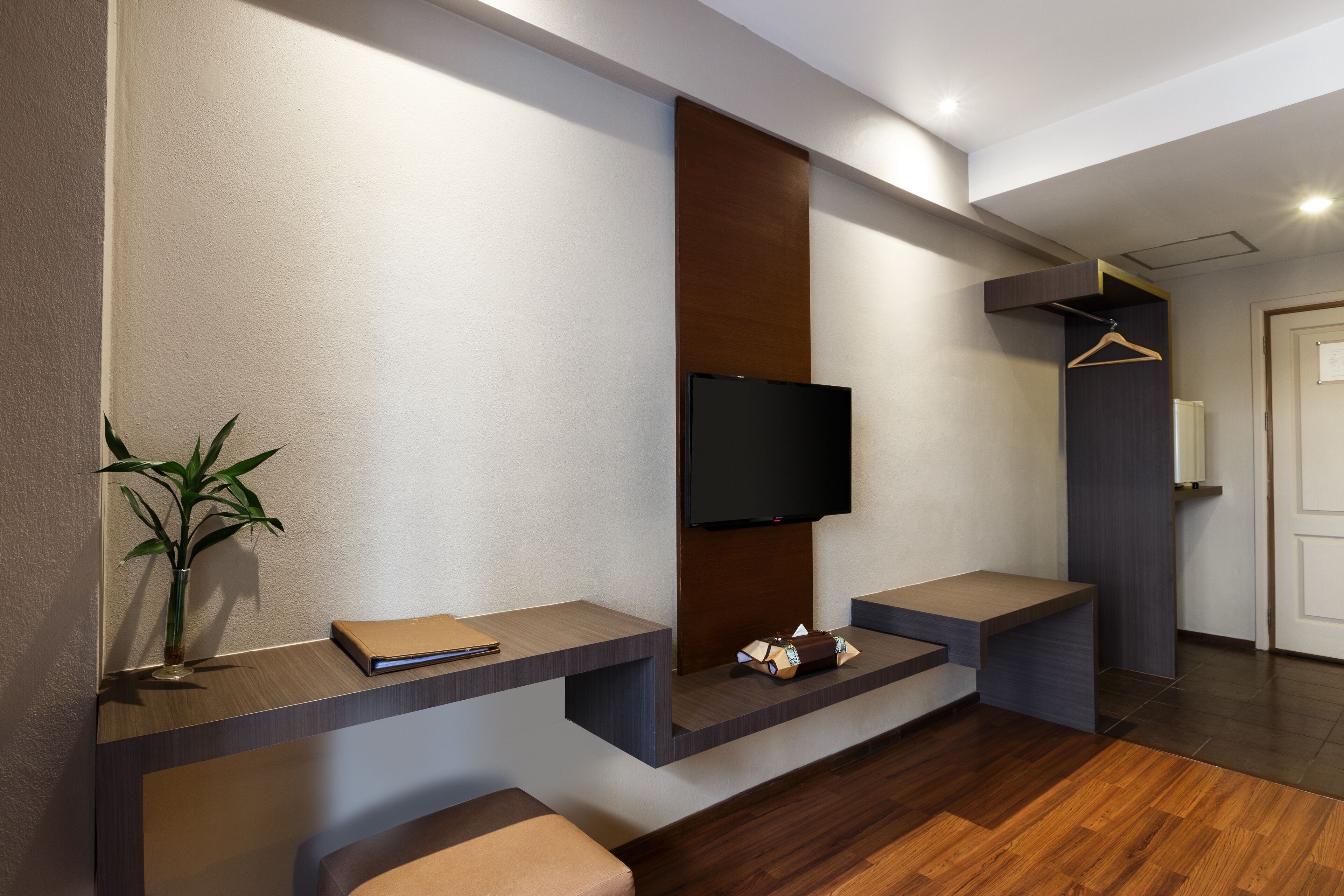 A modern room with a flat-screen TV mounted on a wall, a small table with a book and a plant, and a bench.