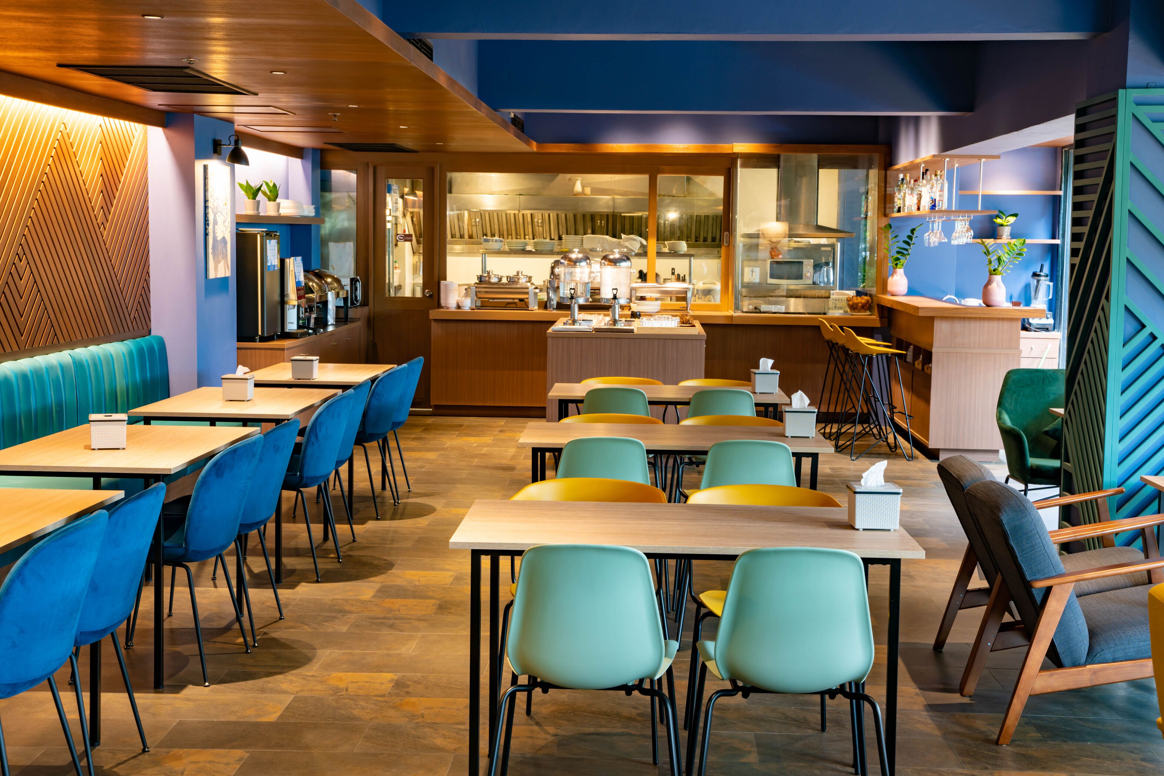 Un restaurante moderno con detalles de madera, sillas azules y amarillas, y una cocina a la vista.