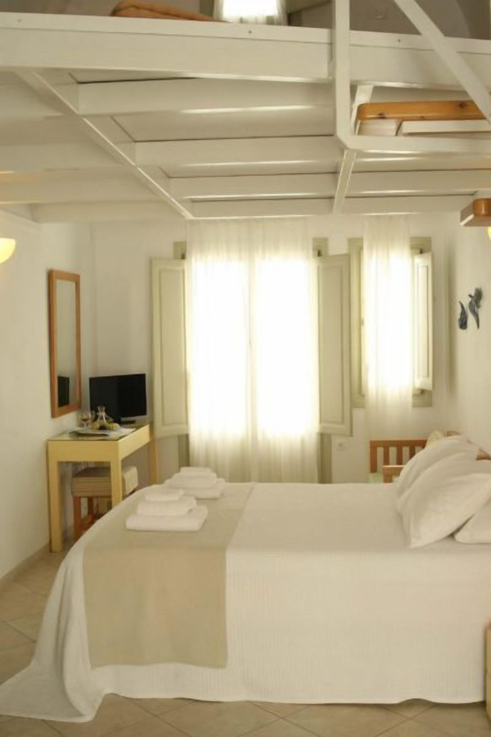 Une chambre d’hôtel avec un lit, un bureau avec une télévision et une grande fenêtre avec des rideaux.