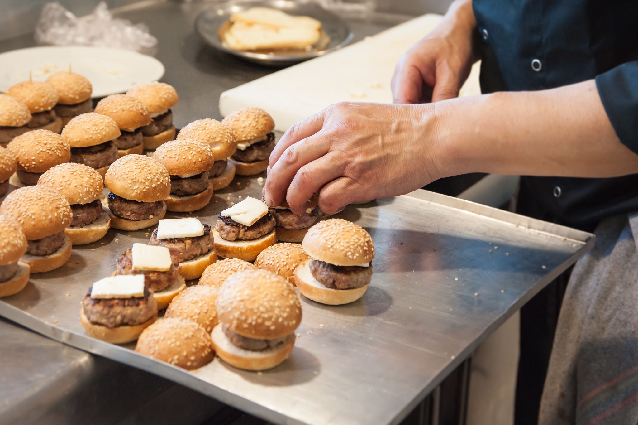 Una persona muntant mini hamburgueses sobre una safata metàl·lica.