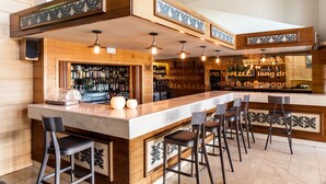 A bar area with a long counter, multiple stools, and hanging pendant lights. - Park-Hotel (Puigcerda)