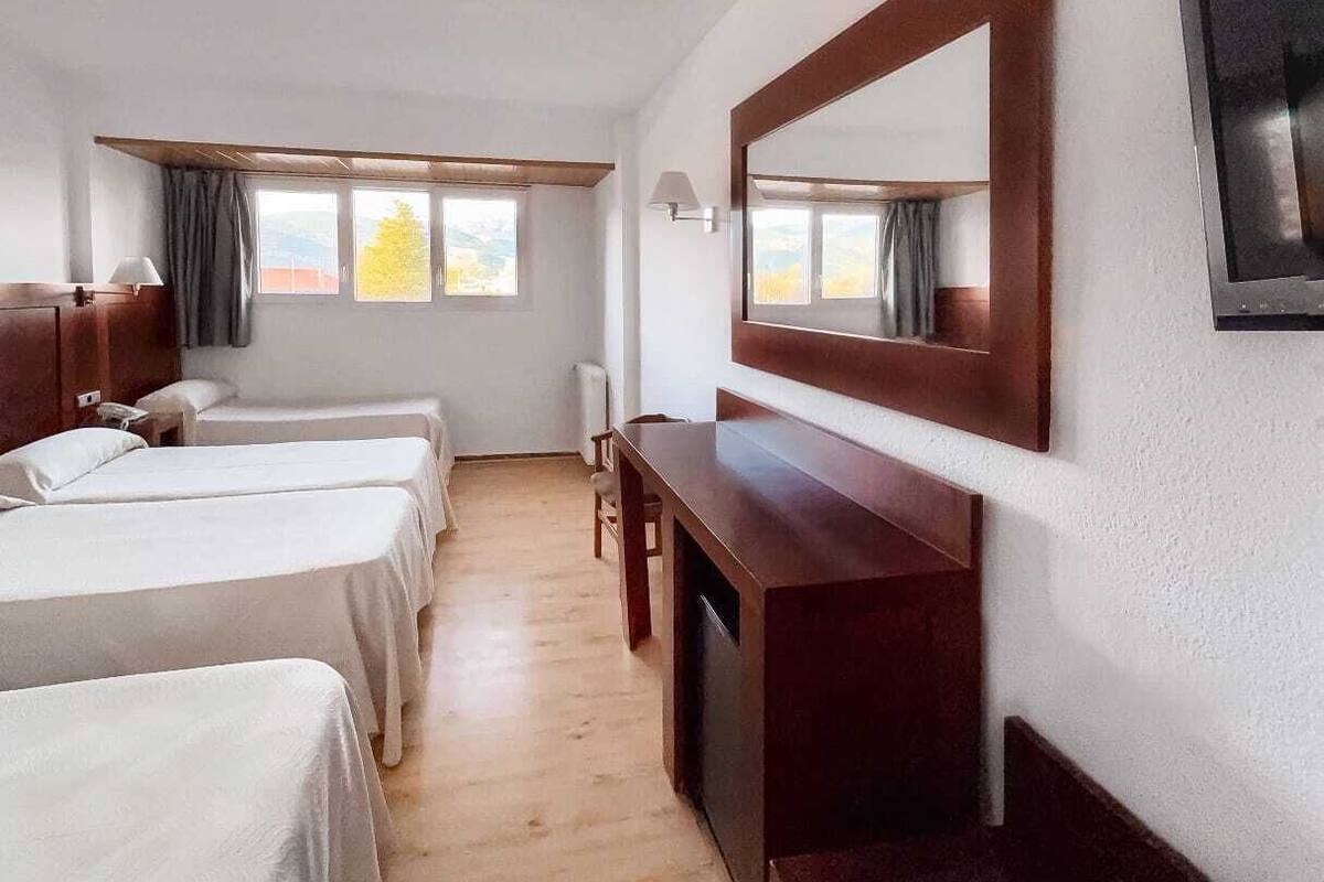A hotel room with two single beds, a desk, a chair, a large mirror, and a window with curtains.