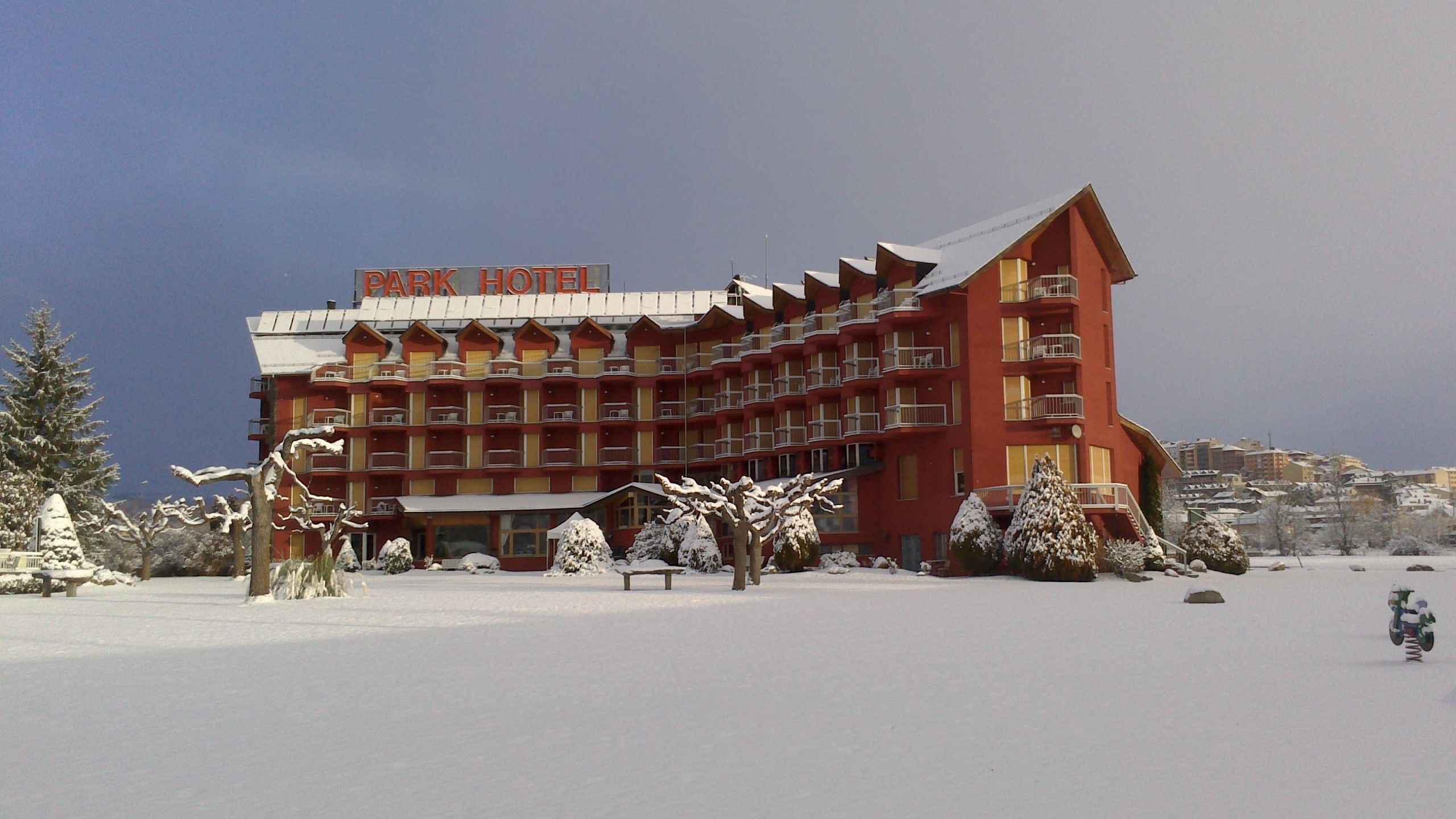 A multi-story hotel with a red facade and balconies, surrounded by snow-covered trees and a clear sky.