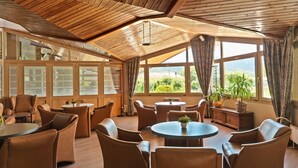 A spacious room with wooden ceiling beams, large windows with curtains, and multiple seating areas with tables and chairs. - Park-Hotel (Puigcerda)