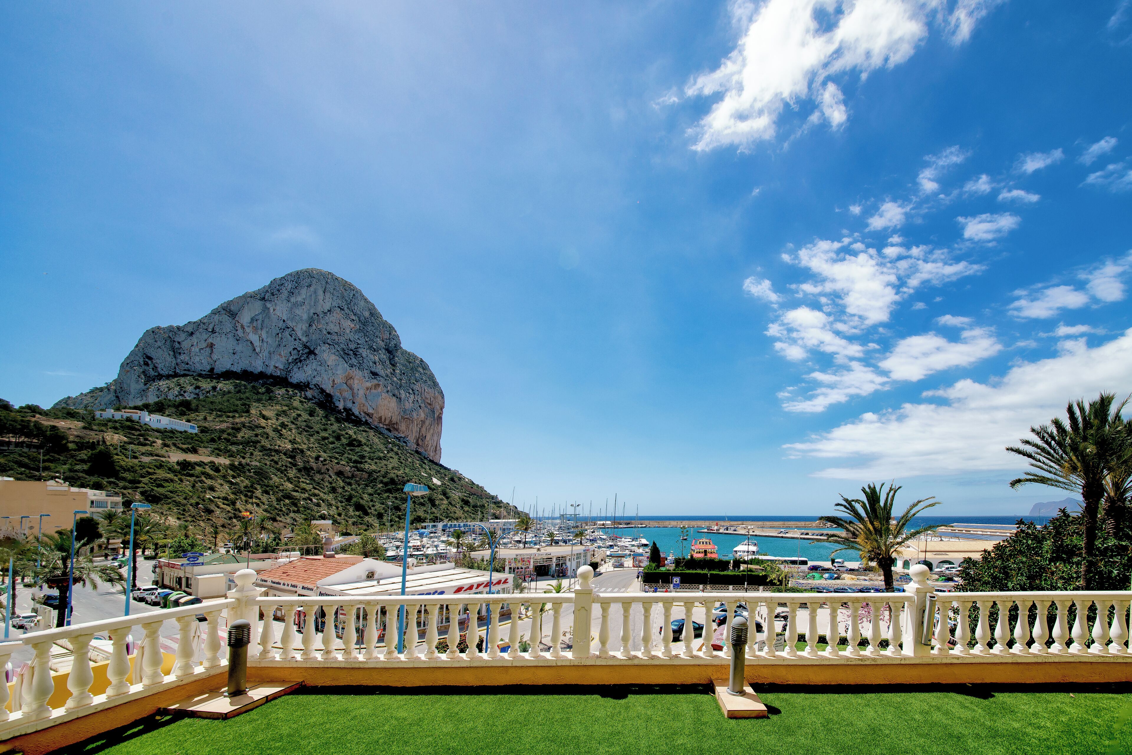 A balcony with a view of a rocky hill, a marina, and a beach.
