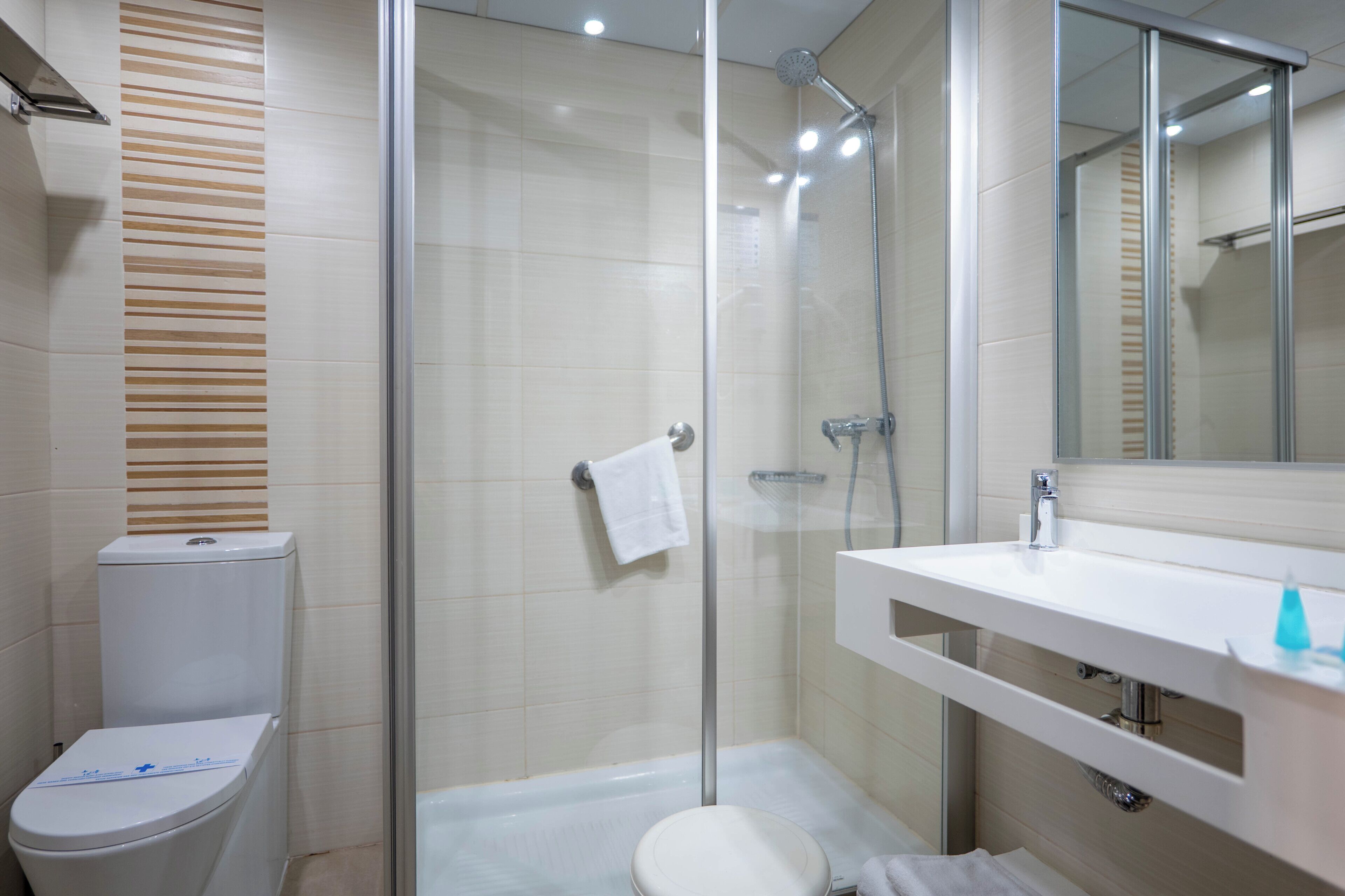 Un baño moderno con cabina de ducha de vidrio, inodoro blanco y lavabo con espejo arriba.