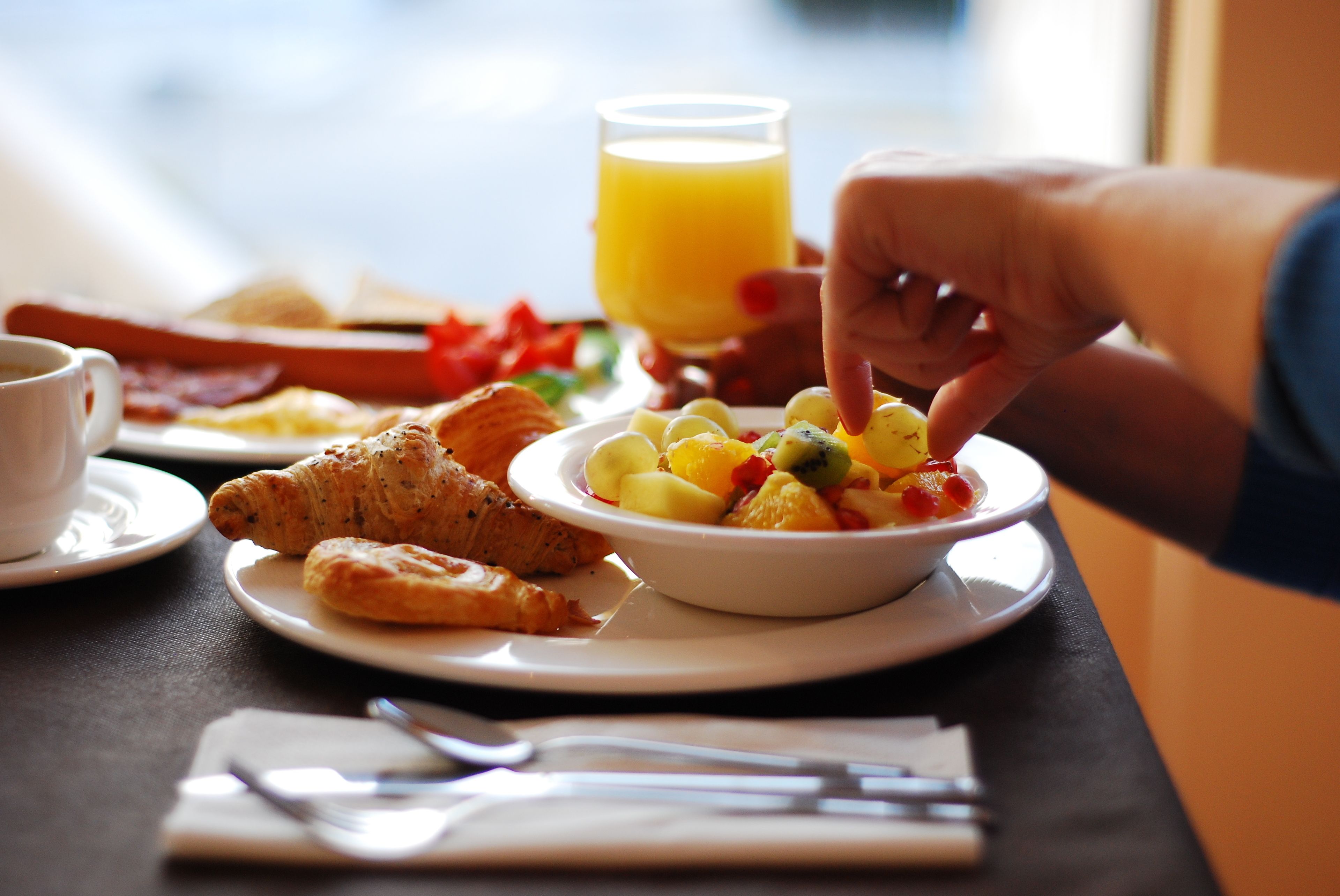 Un desayuno con croissants, un tazón de ensalada de frutas, un vaso de jugo de naranja y una taza de café sobre una mesa.
