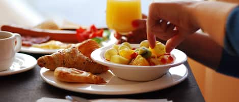 A breakfast setting with croissants, a bowl of fruit salad, a glass of orange juice, and a cup of coffee on a table.