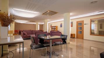 A modern lobby with a glass table, leather chairs, a sofa, and a bookshelf.
