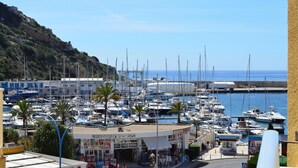 Un puerto deportivo con numerosas embarcaciones amarradas, una estación de servicio y un paisaje montañoso al fondo.