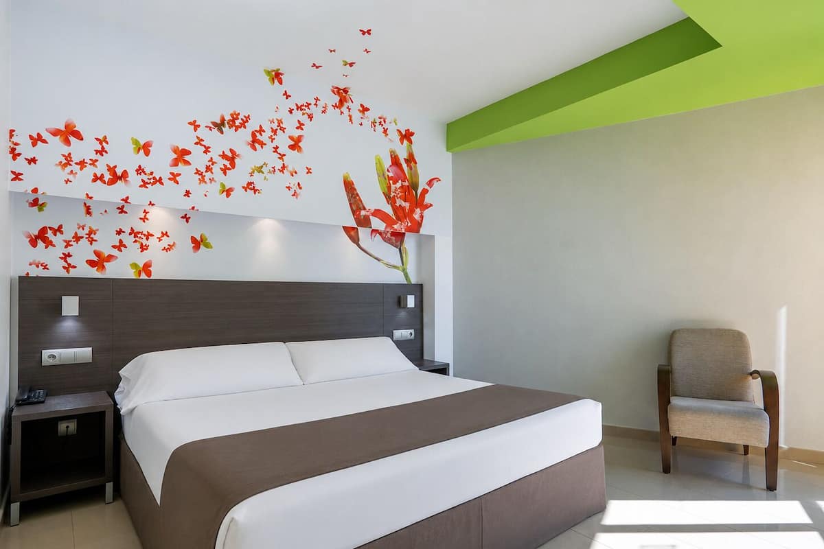 A modern hotel room with a large bed, a nightstand, a chair, and a decorative wall with red flowers and butterflies.