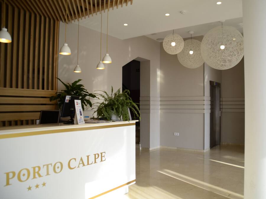 A reception area with a white counter labeled "PORTO CALPE" and hanging pendant lights.