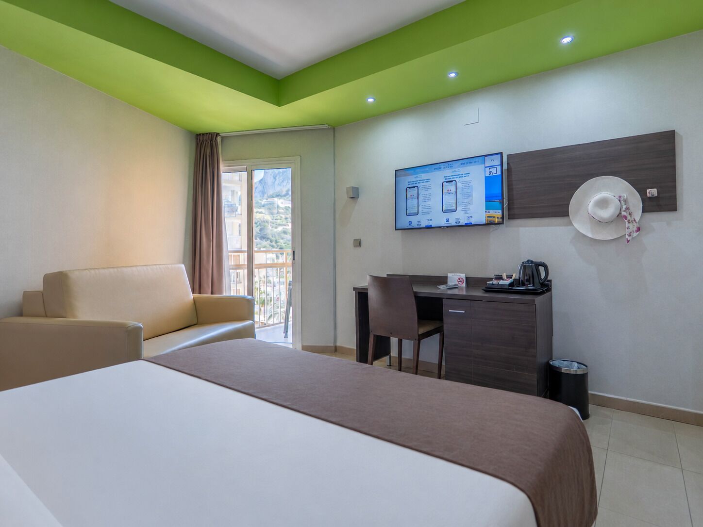 Habitación de hotel con cama, escritorio, silla, televisor y balcón con vistas.
