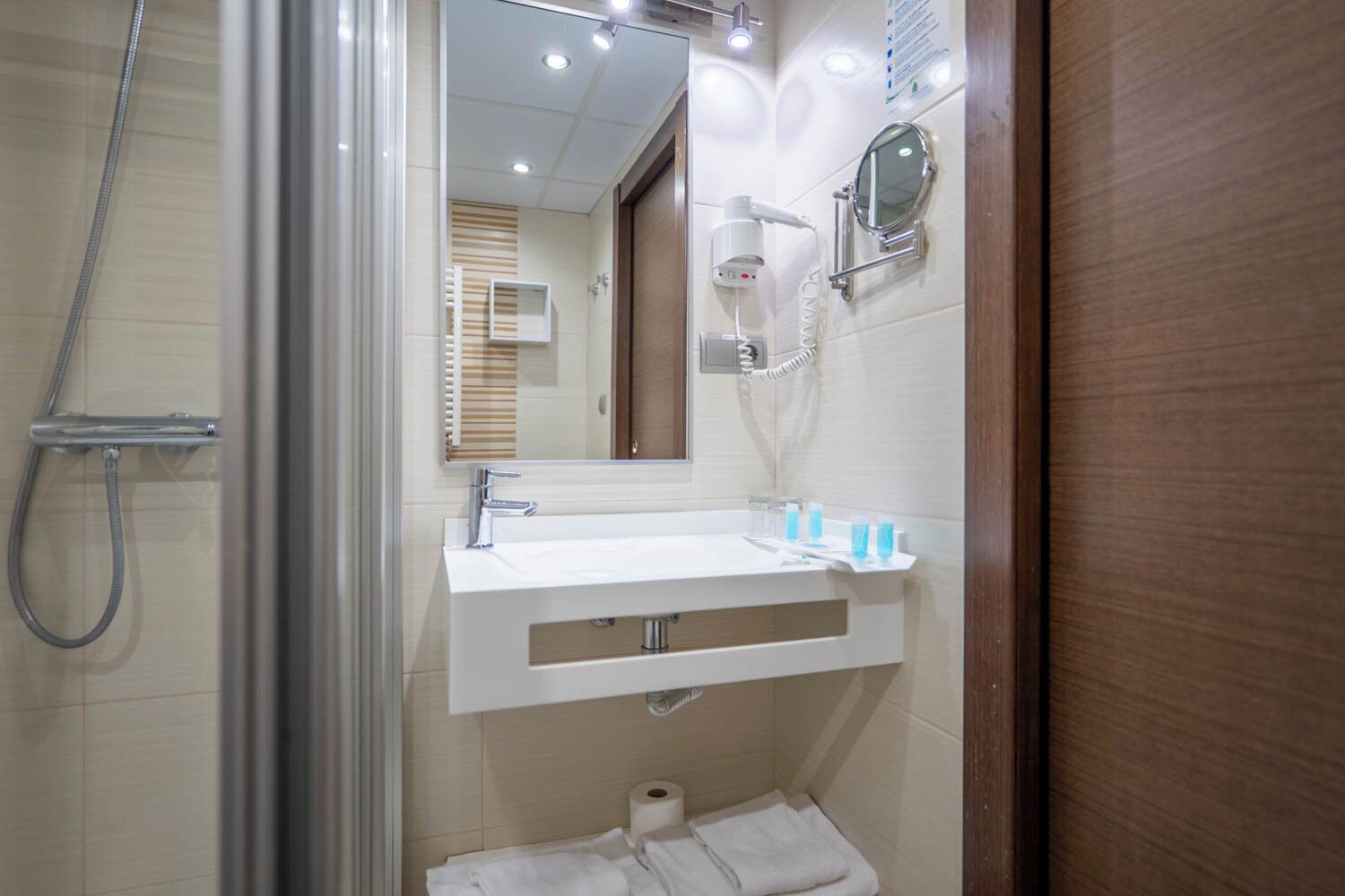 Uma casa de banho moderna com chuveiro, lavatório com espelho e suporte para toalhas.