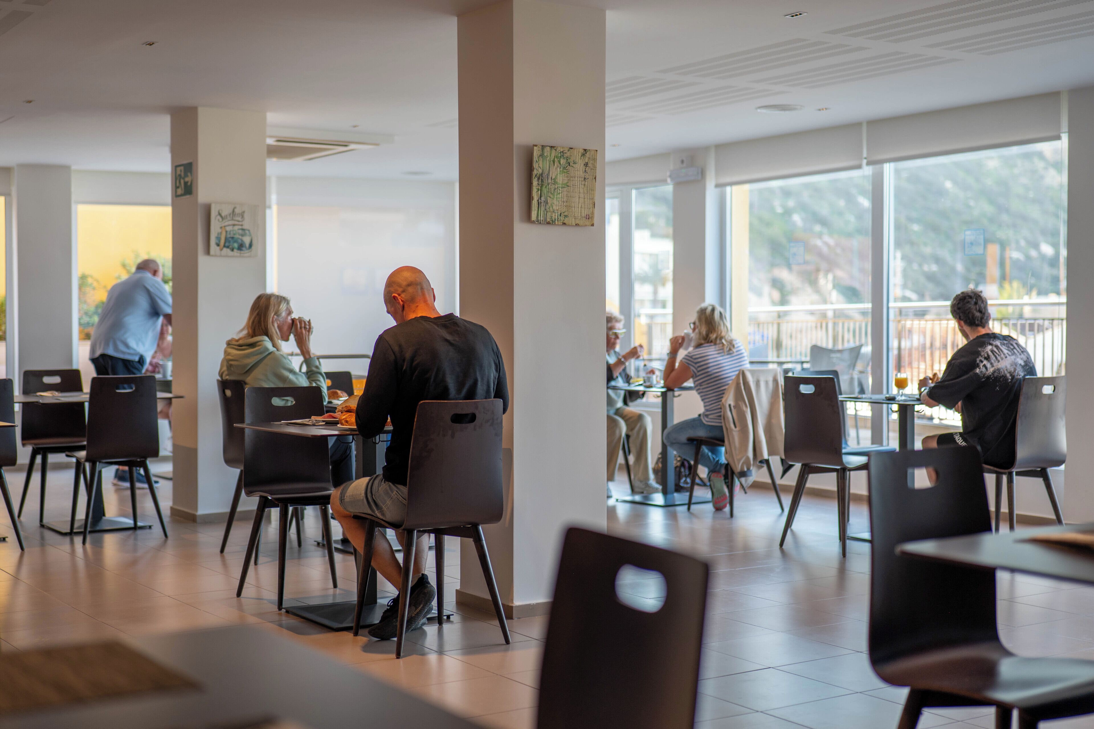 Un espace de restauration intérieur moderne, avec des chaises et des tables noires, de grandes fenêtres et un design épuré et minimaliste.