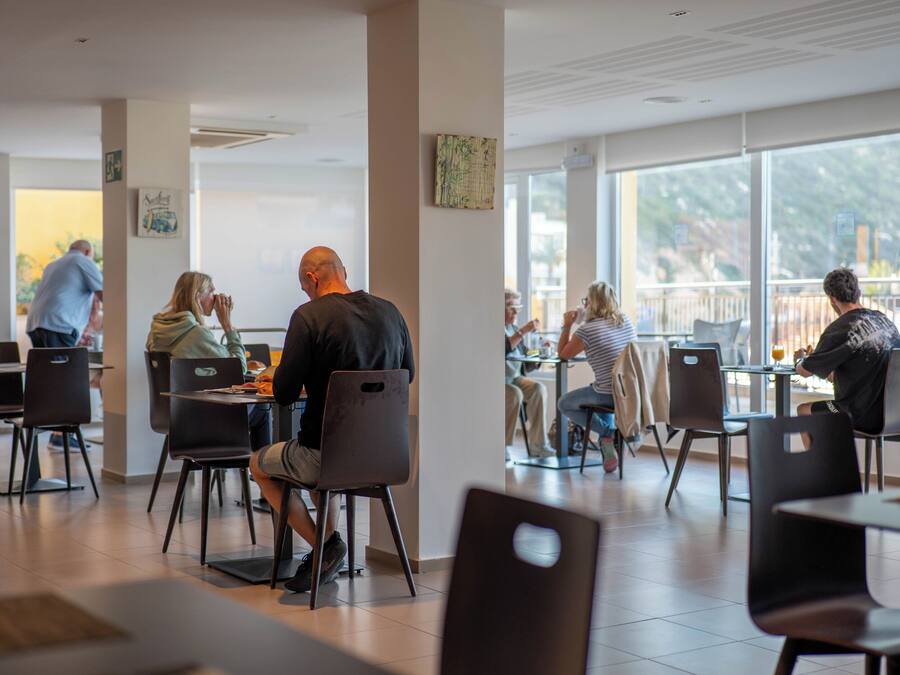 Un comedor interior moderno con sillas y mesas negras, ventanas amplias y un diseño limpio y minimalista.
