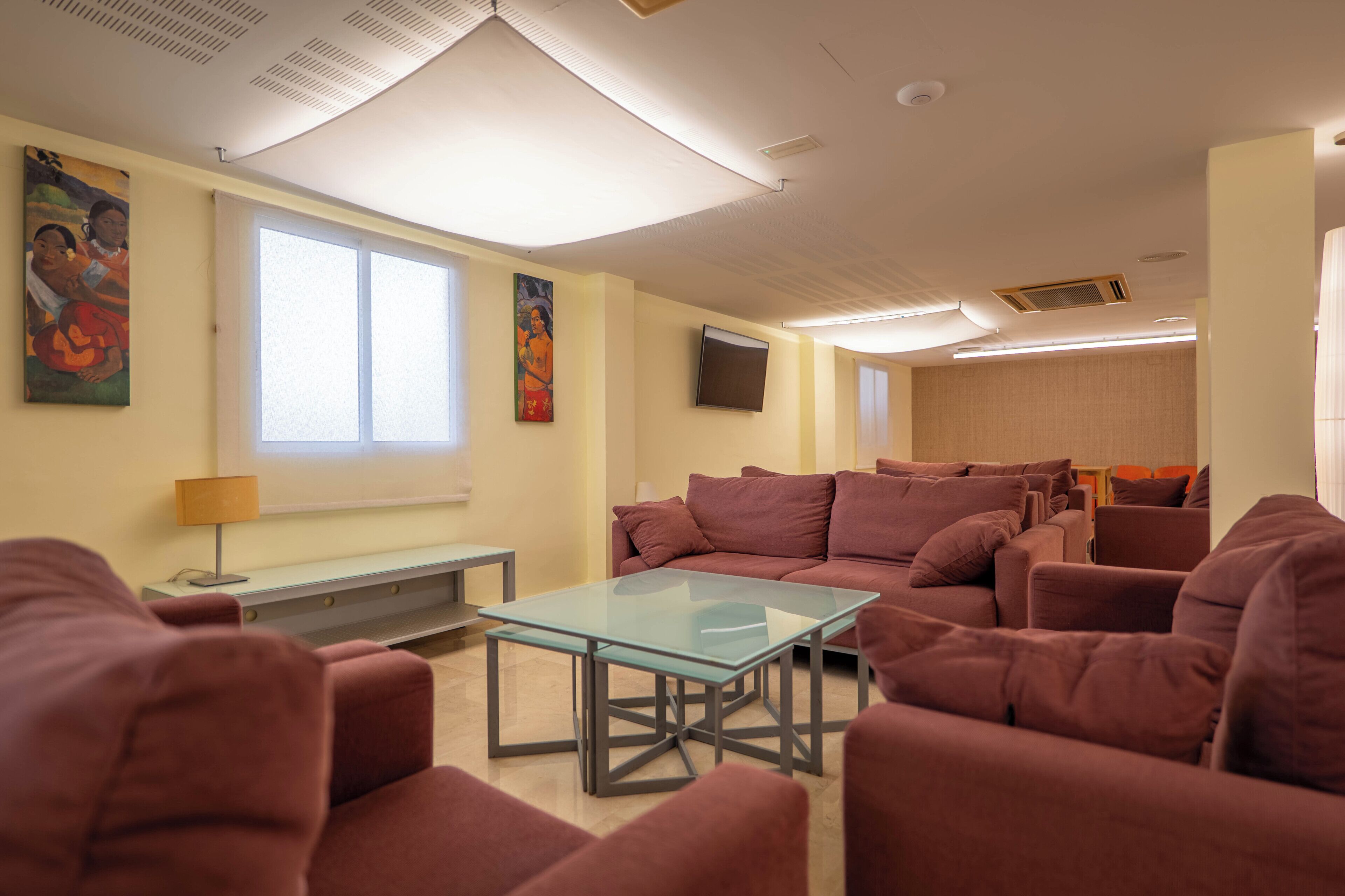 A room with a glass-top table, multiple sofas, a flat-screen TV, and artwork on the walls.